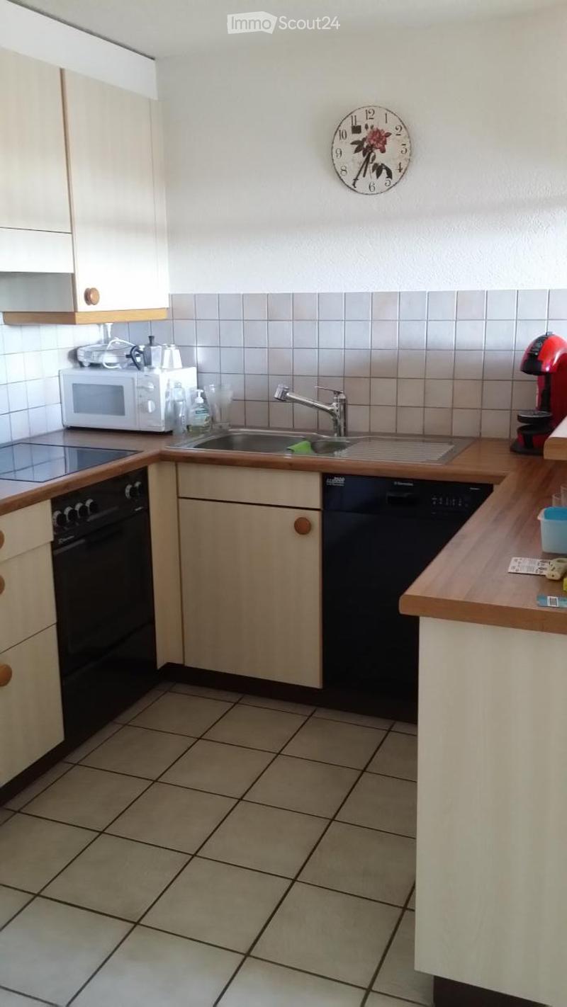 Compact kitchen with tiled walls, wooden cabinets, microwave, sink, and a clock on the wall.