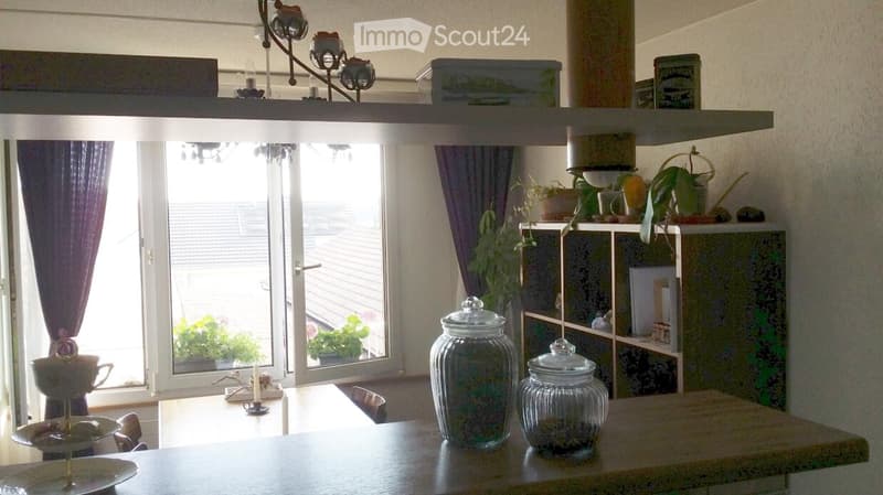 A cozy dining area with a wooden table, chairs, shelves, and decorative items including jars and plants.