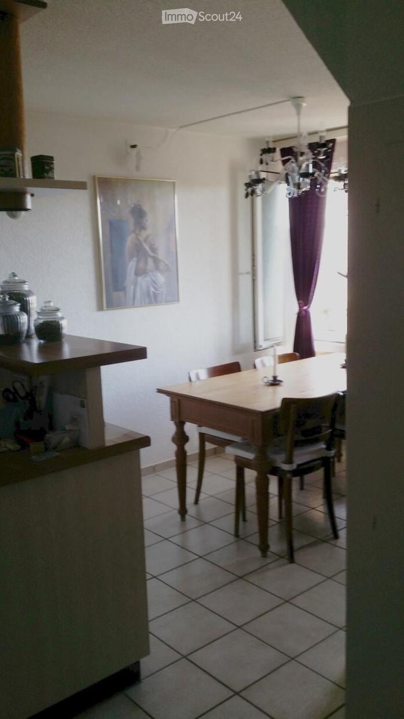 A cozy dining area with a wooden dining table and chairs, a chandelier, a picture frame on the wall, and a curtained window.