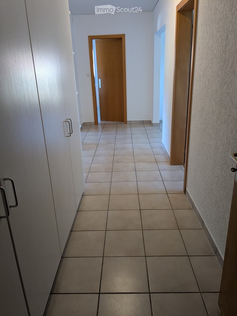 Empty hallway with tiled floor, white walls, and wooden doors on both sides.
