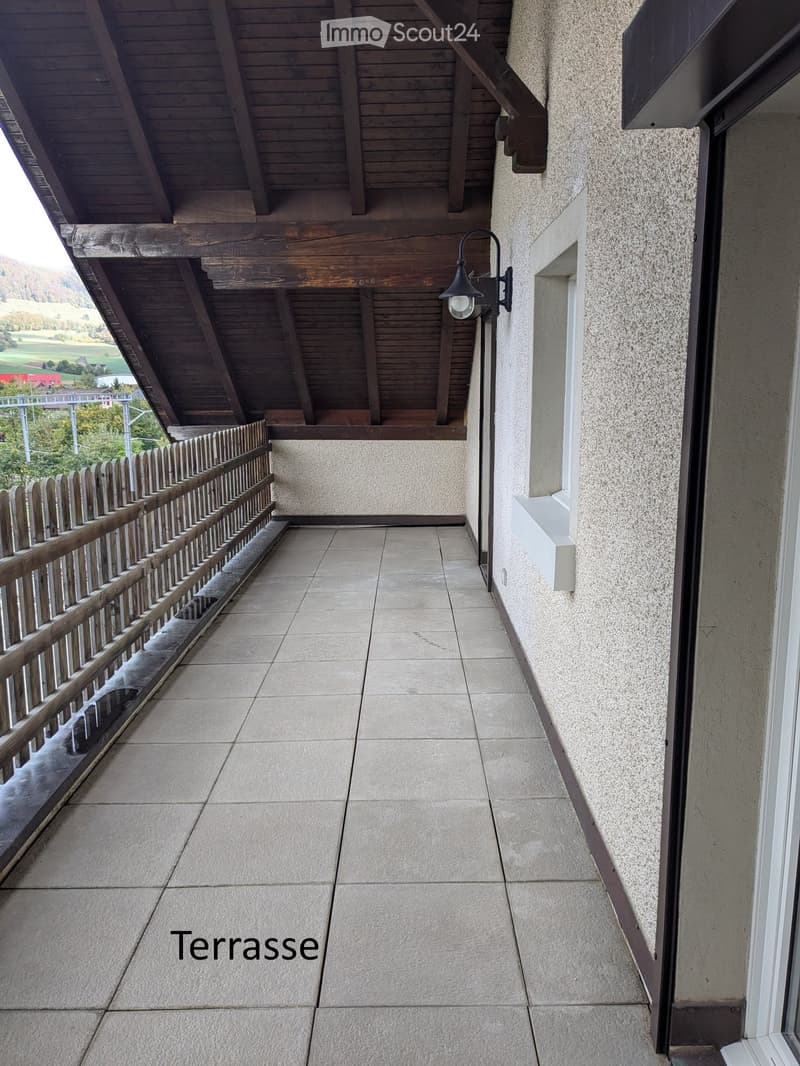 Balcony with tiled floor, wooden railing, and a view of a green landscape.