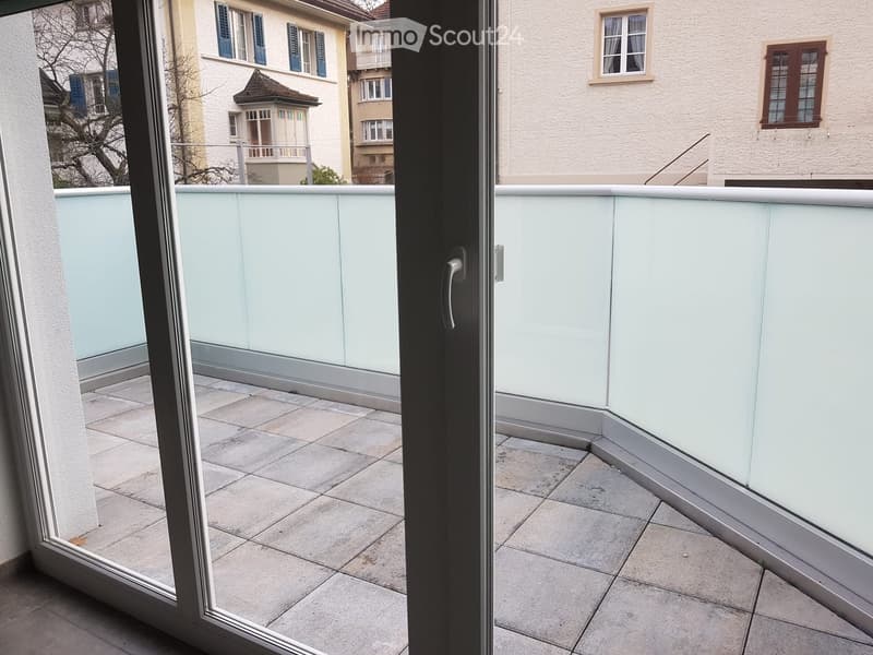 Balcony with tiled floor, glass railing, and view of neighboring buildings.