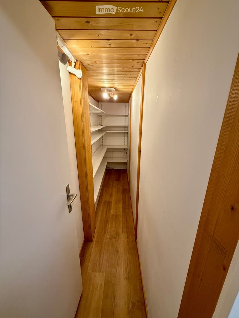 A narrow wooden hallway with white walls, wooden ceiling, and built-in shelving on one side.