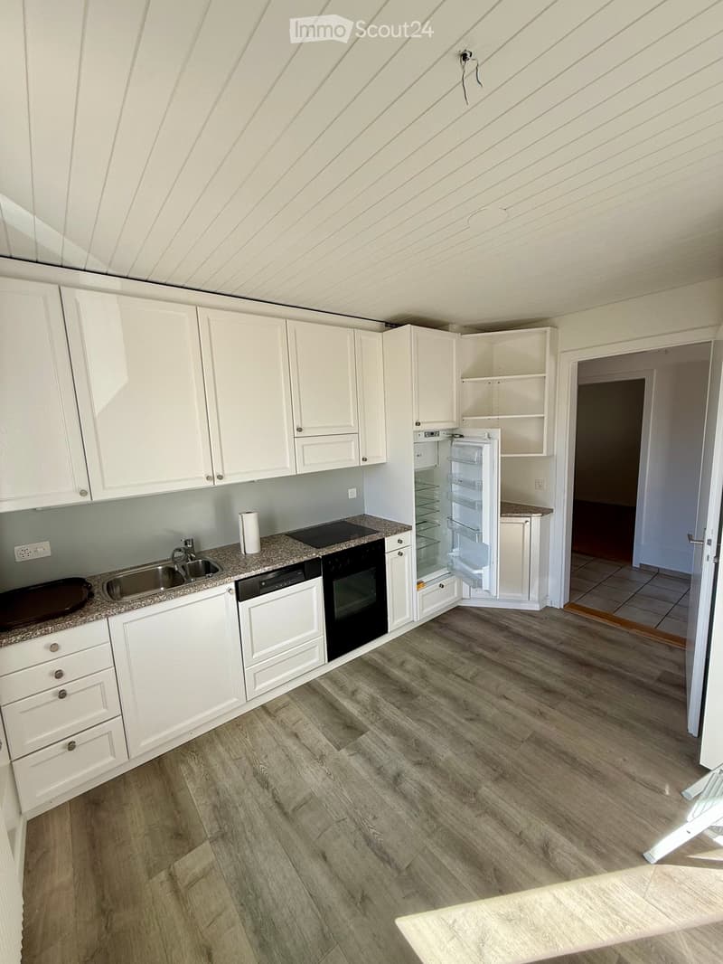 Modern kitchen with white cabinets, granite countertop, stainless steel sink, and built-in appliances including a fridge, oven, and dishwasher. Wooden flooring and open shelving visible.