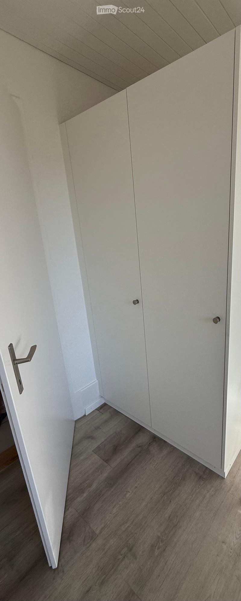 Empty room with light-colored walls, wooden flooring, and white built-in cabinets.