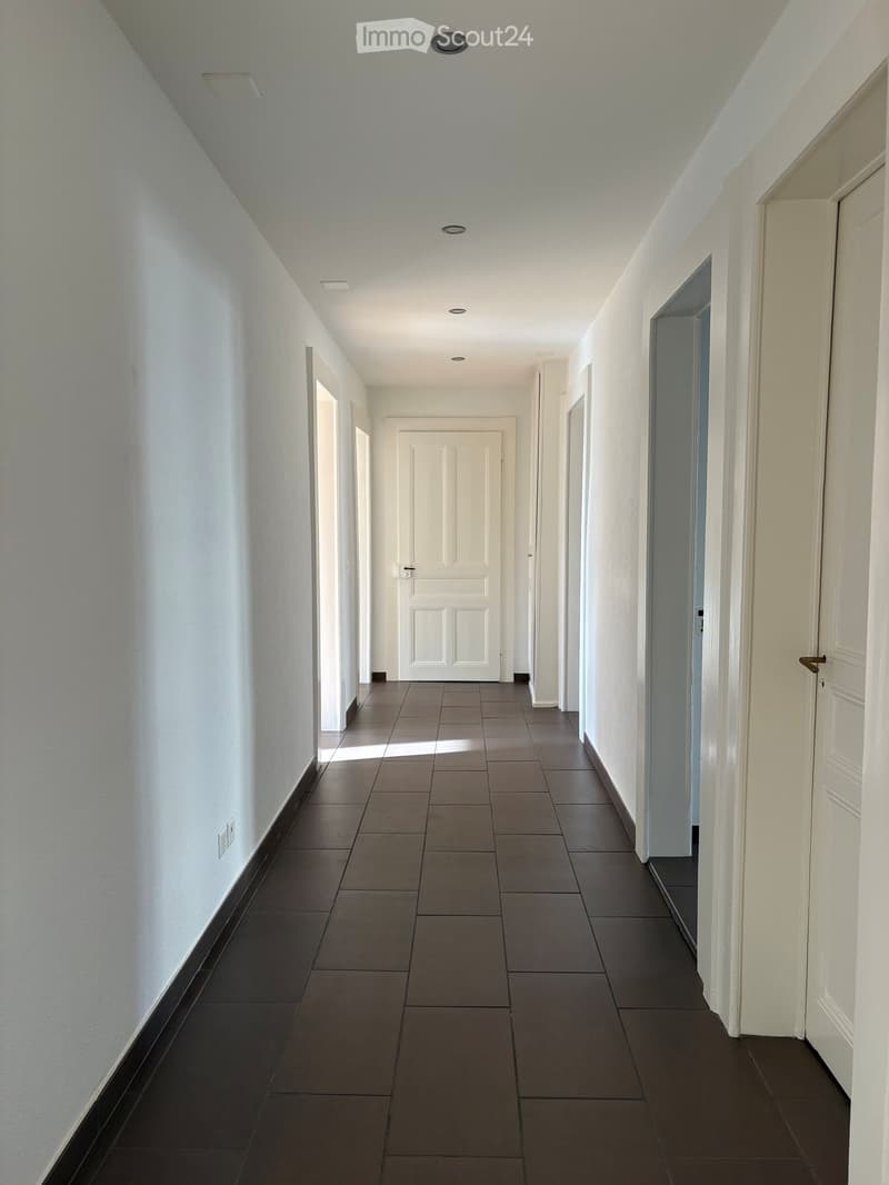 Empty hallway with white walls, dark tiled floor, and several white doors on both sides.