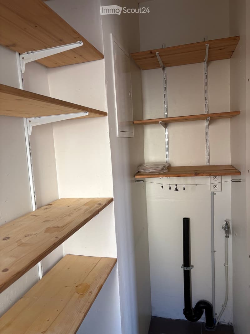 Empty hallway with wooden shelves mounted on the walls, white walls, and visible pipes and electrical outlets.