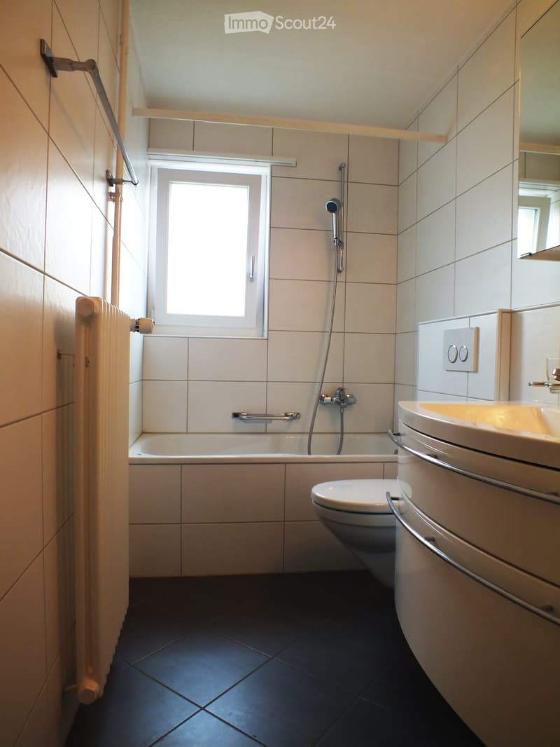 Modern bathroom with white tiles, dark tiled floor, bathtub, toilet, sink, mirror, and showerhead.