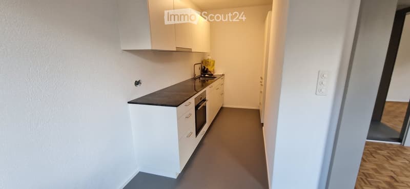 Modern kitchen with white cabinets, black countertop, sink, and oven. The floor is gray, and the walls are white.