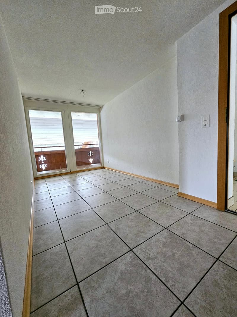 Empty hallway with tiled floor, light-colored walls, and a sliding glass door leading to a balcony.