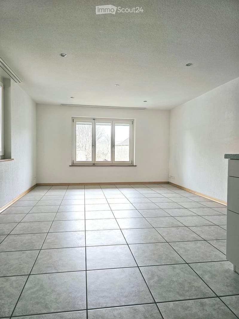 Empty room with tiled floor, white walls, and a large window with white frame. No furniture or equipment present.