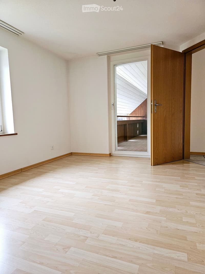 Empty room with light wooden flooring, white walls, and a sliding glass door leading to a balcony area.