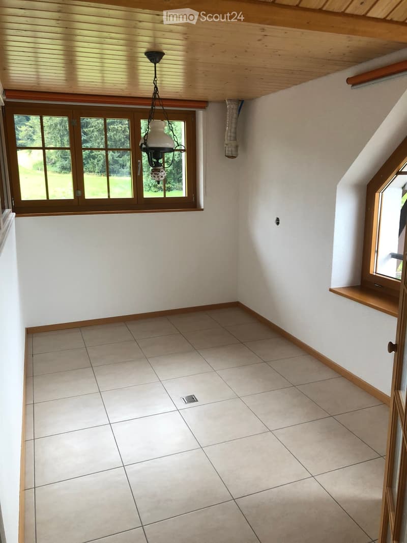 Empty room with tiled floor, white walls, wooden trim, large window with wooden frame, and a hanging light fixture.
