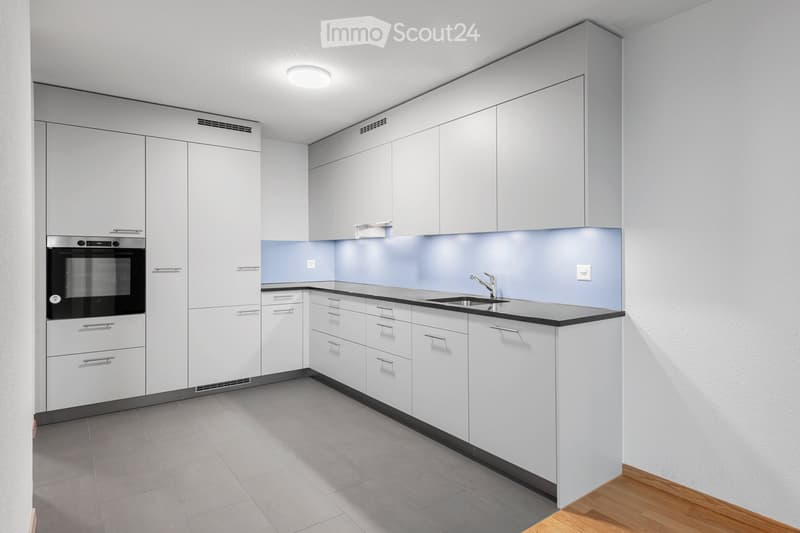 Modern kitchen with white cabinets, black countertops, and stainless steel appliances including an oven and sink.