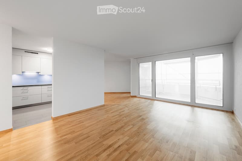 Empty room with light wooden flooring, white walls, and large glass sliding doors leading to a balcony.