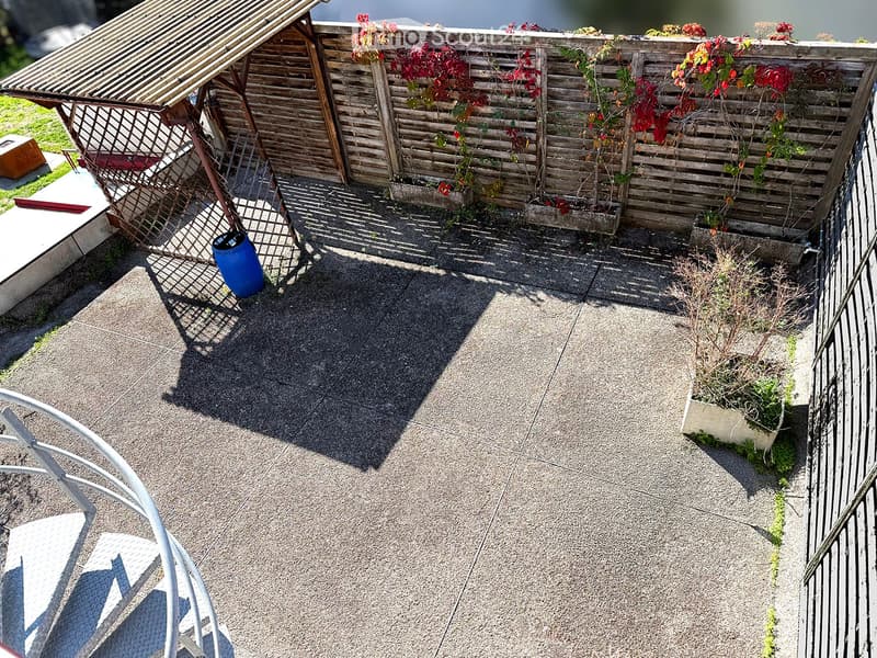 Roof terrace with wooden fence, climbing plants, small seating area, and a blue barrel.