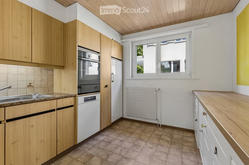 Modern kitchen with light wooden cabinets, stainless steel sink, oven, dishwasher, and a window providing natural light.