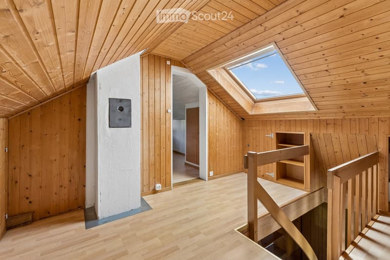 Bright, wooden-floored attic space with exposed wooden beams, skylight windows, and a small wooden staircase leading downwards.