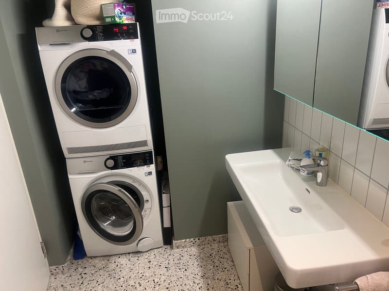 Bathroom with a white sink, modern faucet, and a stacked washing machine and dryer unit.