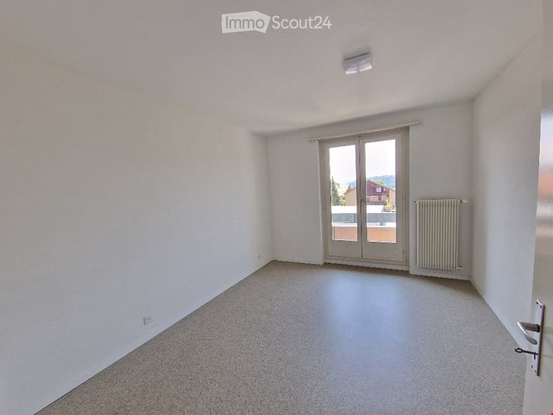 Empty room with white walls, carpeted floor, sliding glass door leading to a balcony, and a radiator on the wall.