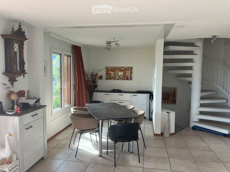 Bright dining area with a black table, beige chairs, white cabinets, and a staircase leading upwards.