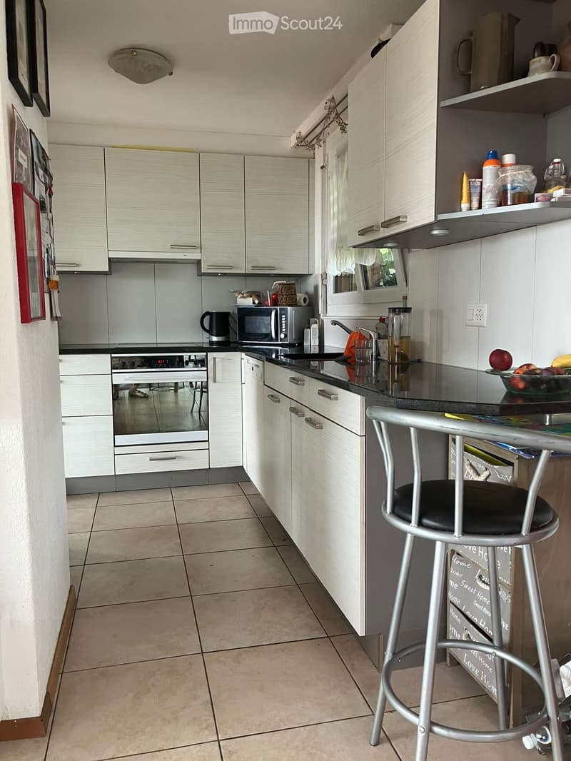 Modern kitchen with white cabinets, black countertops, and stainless steel appliances. Includes a microwave, oven, sink, and a bar stool.