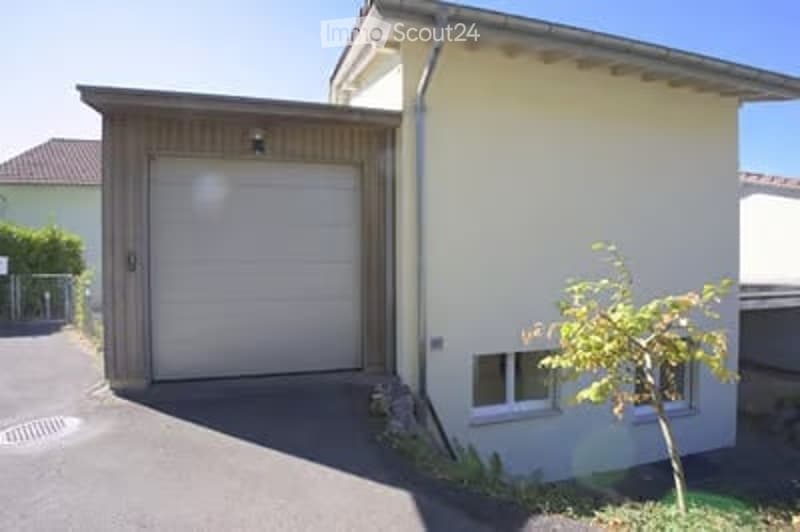 Single-story house with a garage, beige exterior, and small garden area.