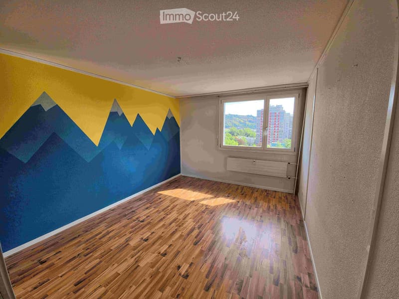 Empty room with wooden flooring, large window, and colorful mountain mural on one wall.