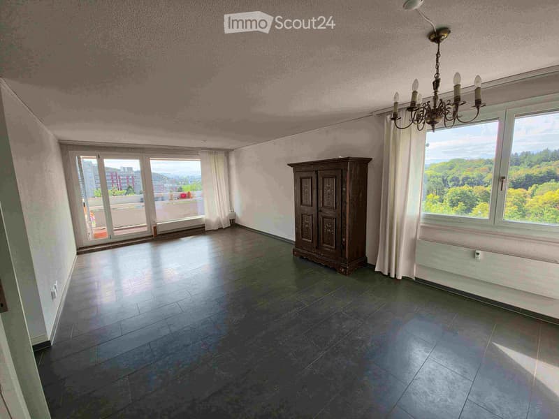 Empty room with large windows, a cabinet, and a chandelier. The room has a tiled floor and is well-lit with natural light.