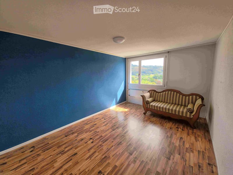 A room with wooden flooring, a blue accent wall, and a window with a scenic view. A striped sofa is positioned near the window.
