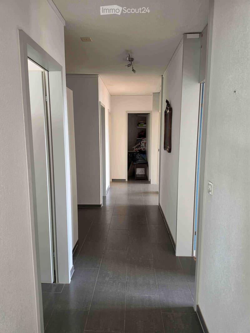 A long, narrow hallway with tiled flooring and white walls, featuring several doors and a small closet area at the end.