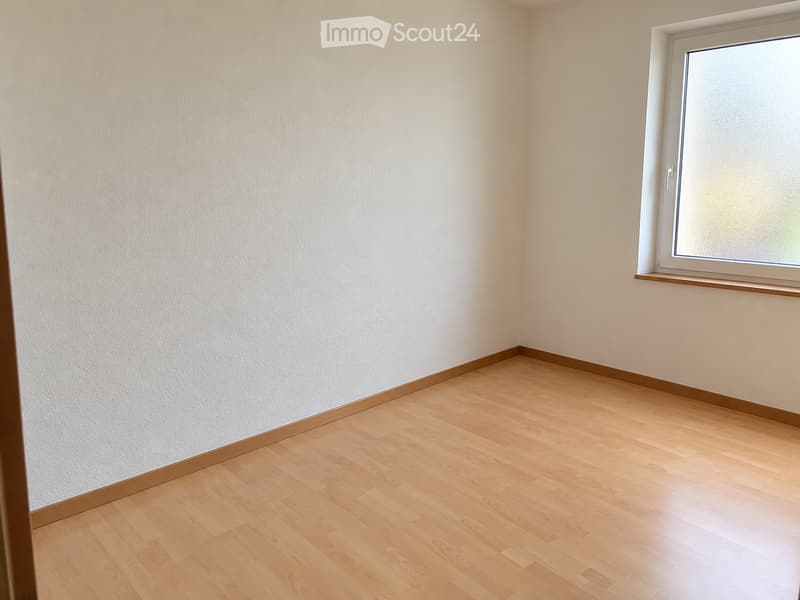 Empty room with light wooden flooring and white walls, featuring a single window with a white frame and a small wooden sill.