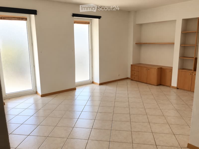 Empty room with tiled floor, built-in wooden cabinets, and large windows with blinds.