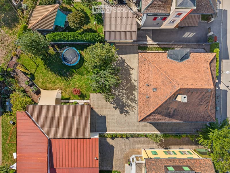 Aerial view of a residential area with multiple houses, gardens, and a trampoline in one of the yards.