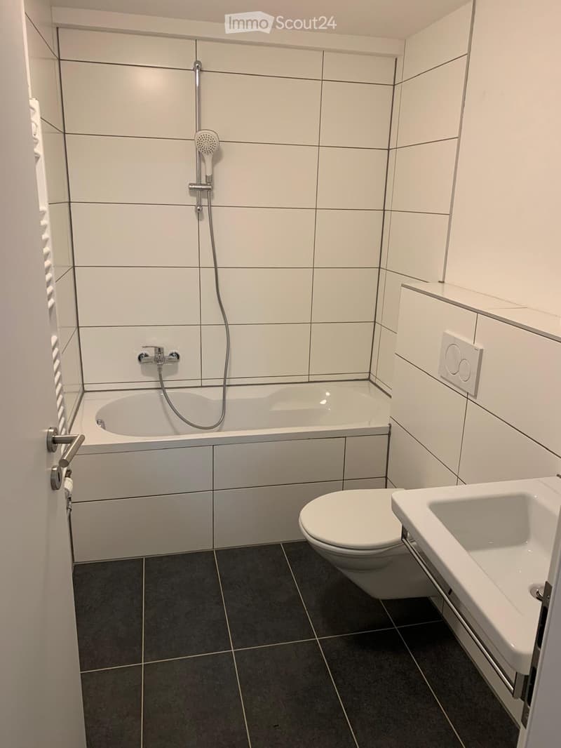 Modern bathroom with white tiles, a bathtub, toilet, sink, and showerhead.