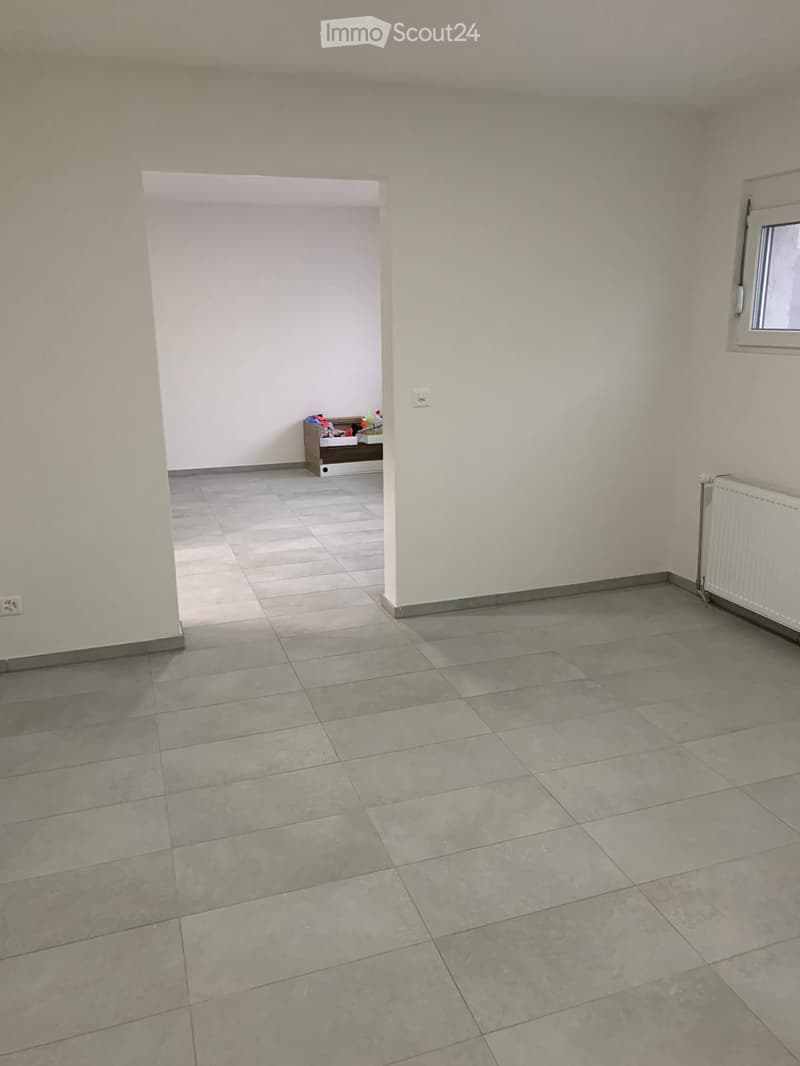 Empty room with tiled floor and white walls, featuring a radiator and a window on the right side.
