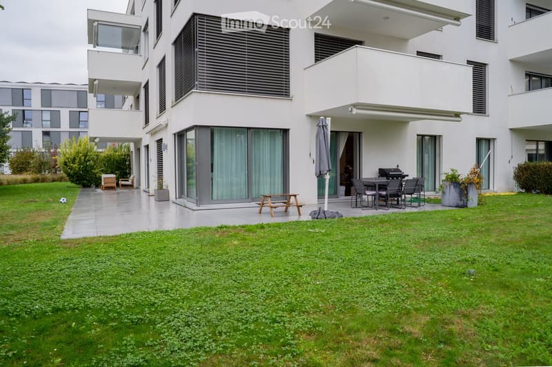 Modern residential building with balconies, patio furniture, and a well-maintained lawn.