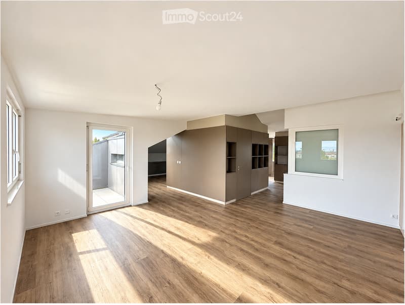 Empty room with wooden flooring, white walls, and large windows allowing natural light. Features a built-in cabinet and a sliding glass door leading to an outdoor area.