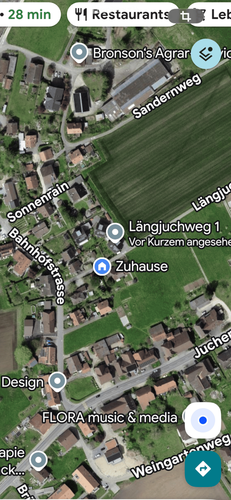 Aerial view of a residential area with multiple houses, green fields, and roads. Markers indicate locations such as 'Zuhause' and 'Längjuchweg 1'.