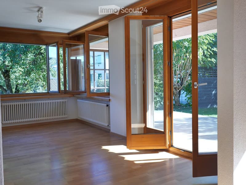 Empty room with wooden flooring, large windows, and radiators along the walls. The space is well-lit with natural light from the windows.