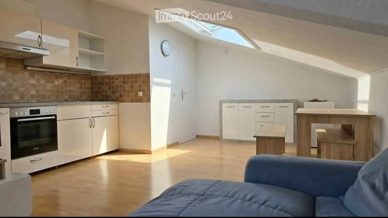 Bright, open-plan living and kitchen area with wooden flooring, white cabinets, a blue sofa, a wooden kitchen island, and a small wooden stool.