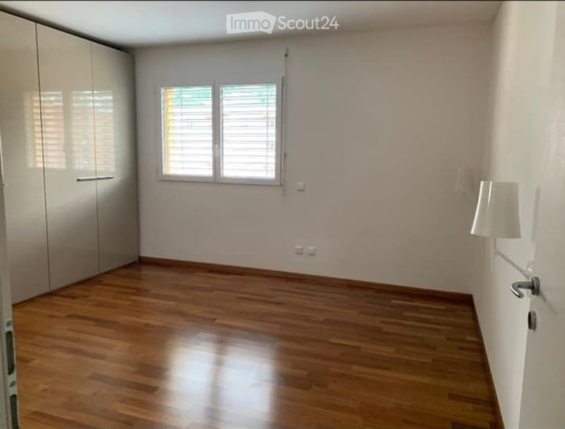 Empty room with wooden flooring, white walls, large window with blinds, and built-in wardrobe.