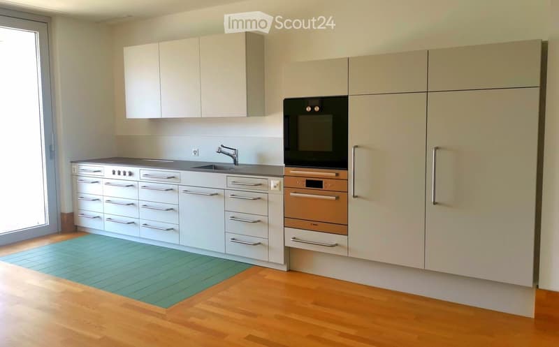 Modern kitchen with light-colored cabinets, stainless steel appliances, and a wooden floor. Features include a sink with a modern faucet, an oven, and multiple cabinets and drawers.