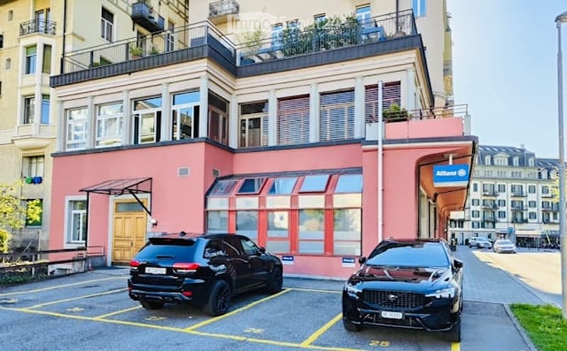 Pink building with large windows and balconies, two black cars parked in front.