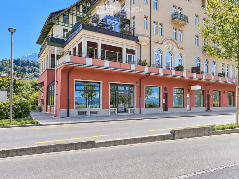 A multi-story building with a mix of modern and traditional architectural elements, featuring balconies, large windows, and a view of mountains in the background.