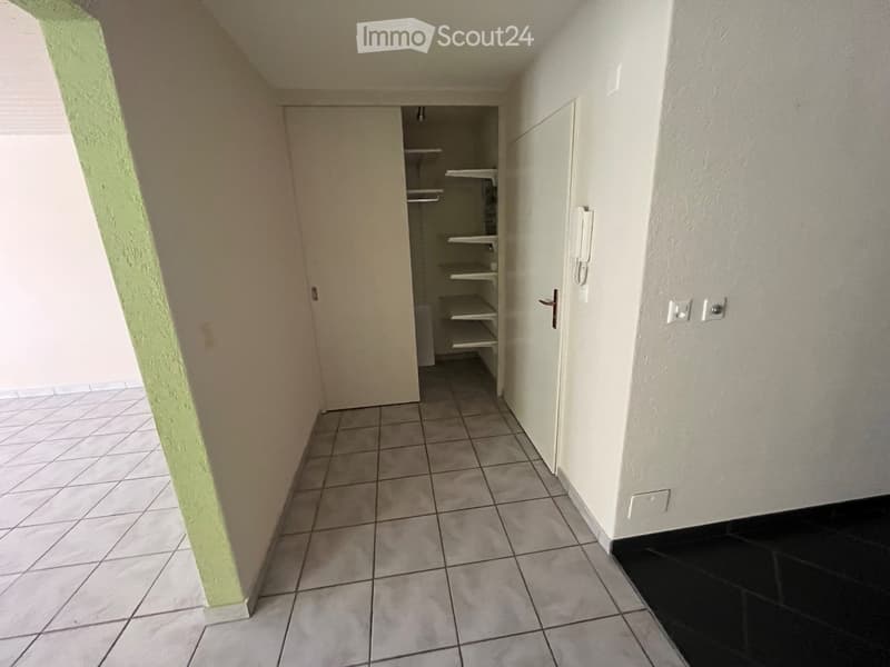 Empty hallway with tiled floor, white walls, and a closet with empty shelves.