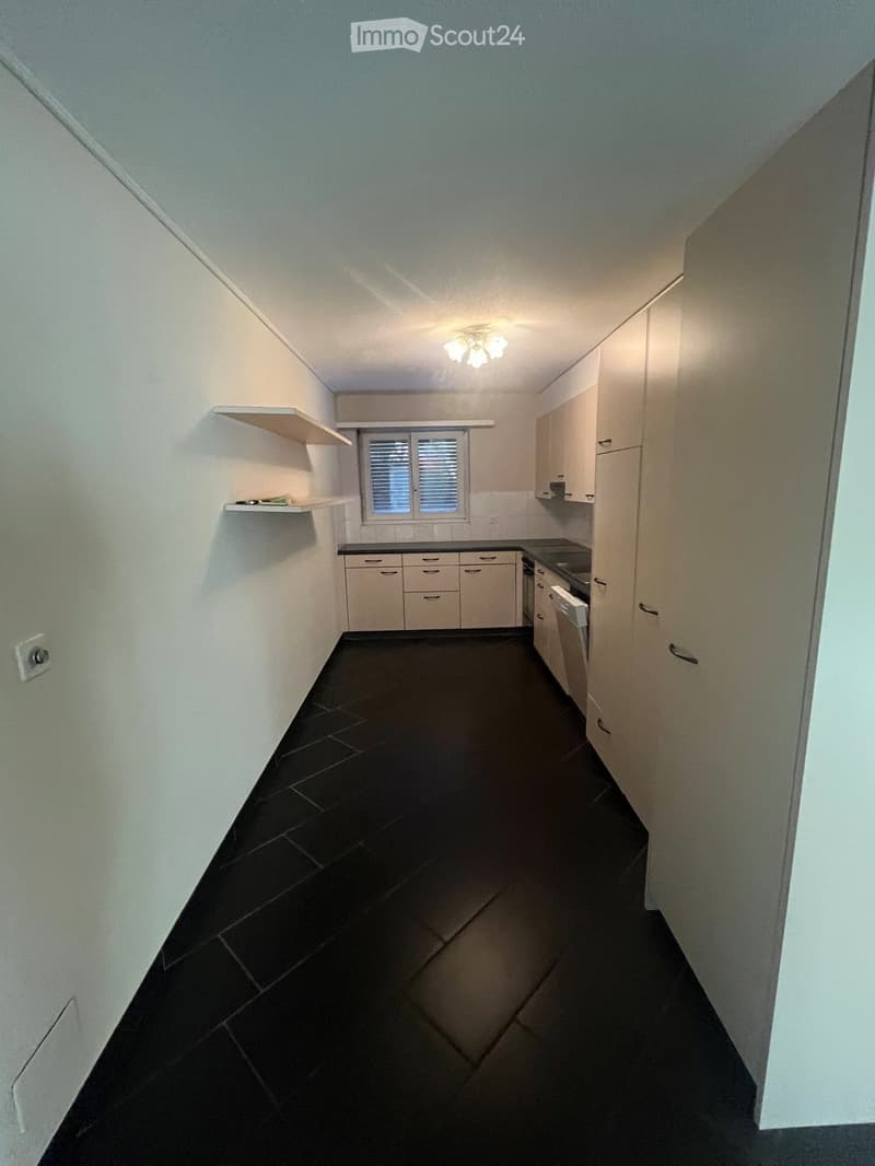 Empty kitchen with white cabinets, black tiled floor, and a window with blinds. No furniture or appliances are present.