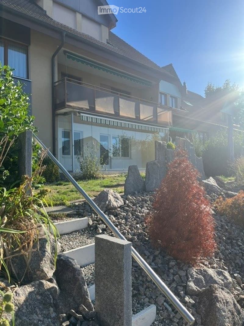 Front yard with decorative rocks, small tree, and a modern house with balconies and large windows.