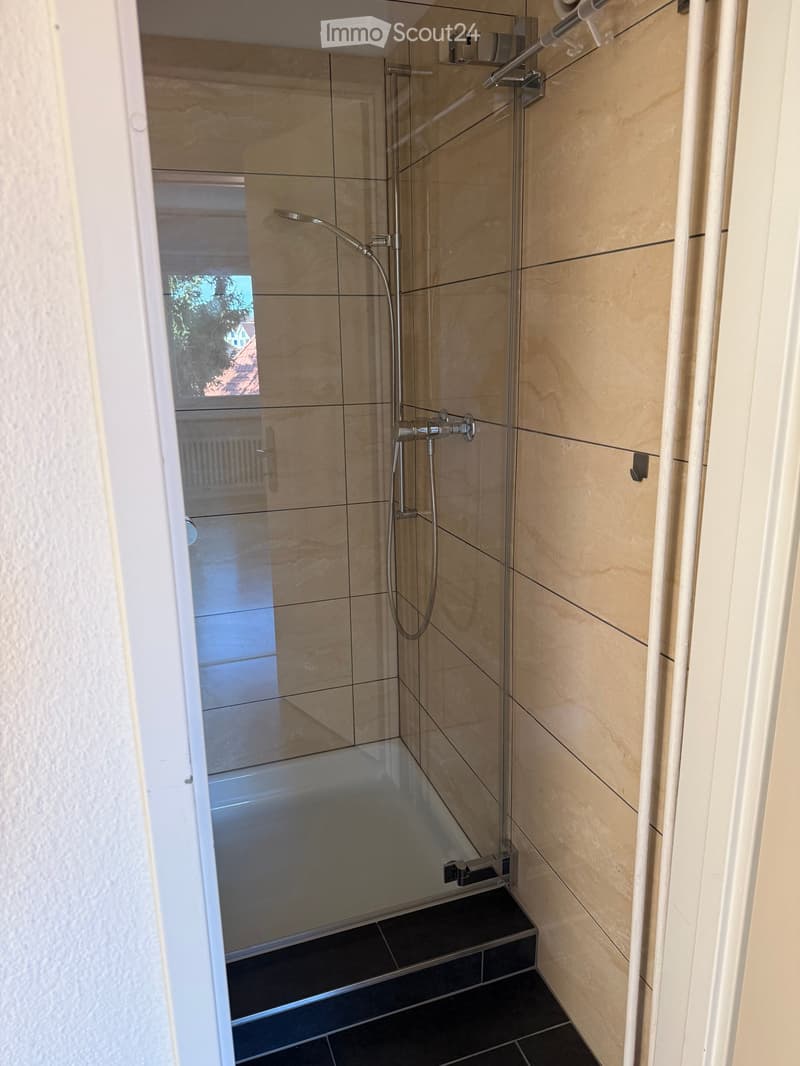 Modern shower area with glass enclosure, beige tiles, and black floor tiles.