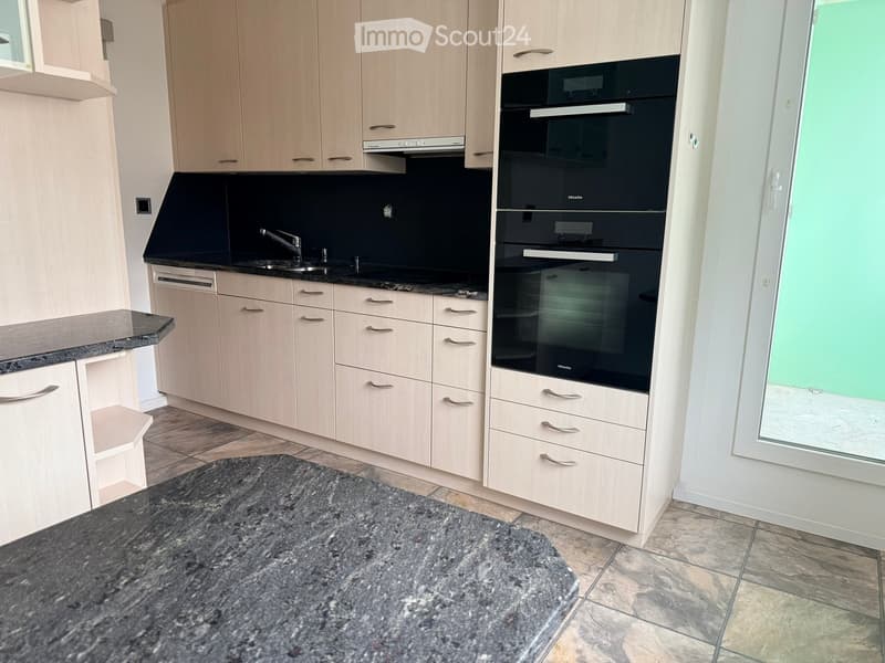 Modern kitchen with light wood cabinets, stainless steel appliances, granite countertop, and tiled floor.